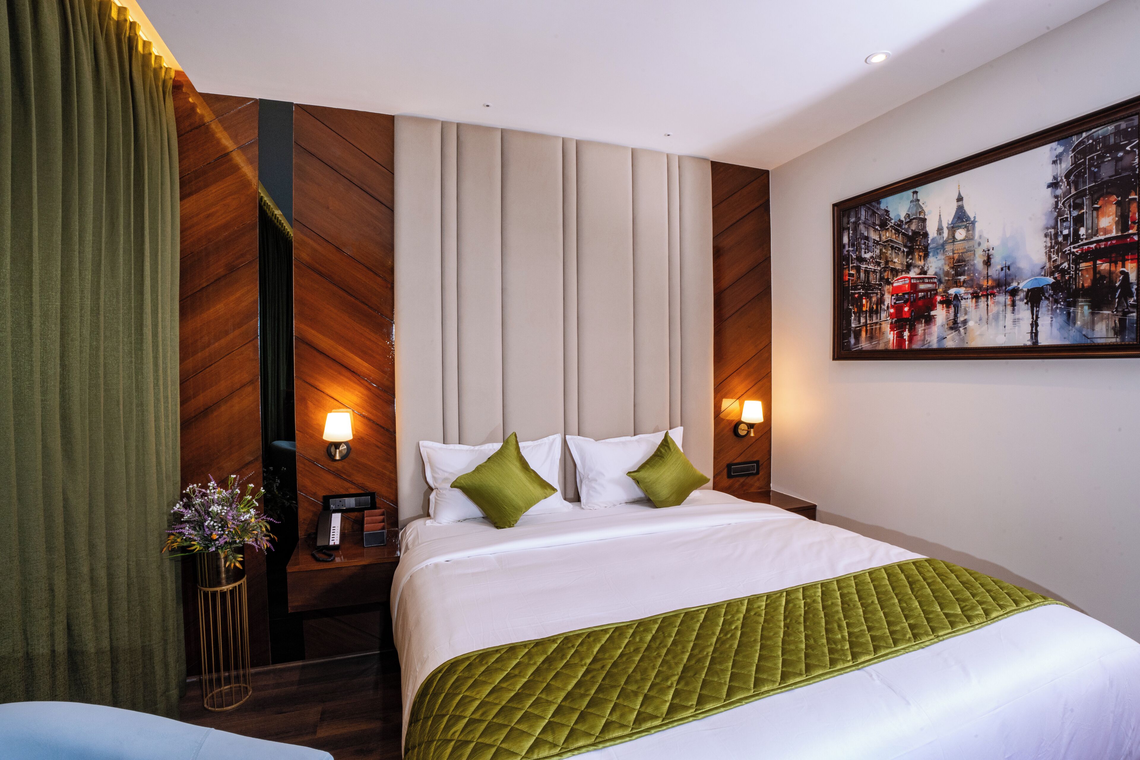 Una camera d'albergo con un letto grande, biancheria verde e bianca, un comodino con una lampada, un quadro al muro e una tenda.