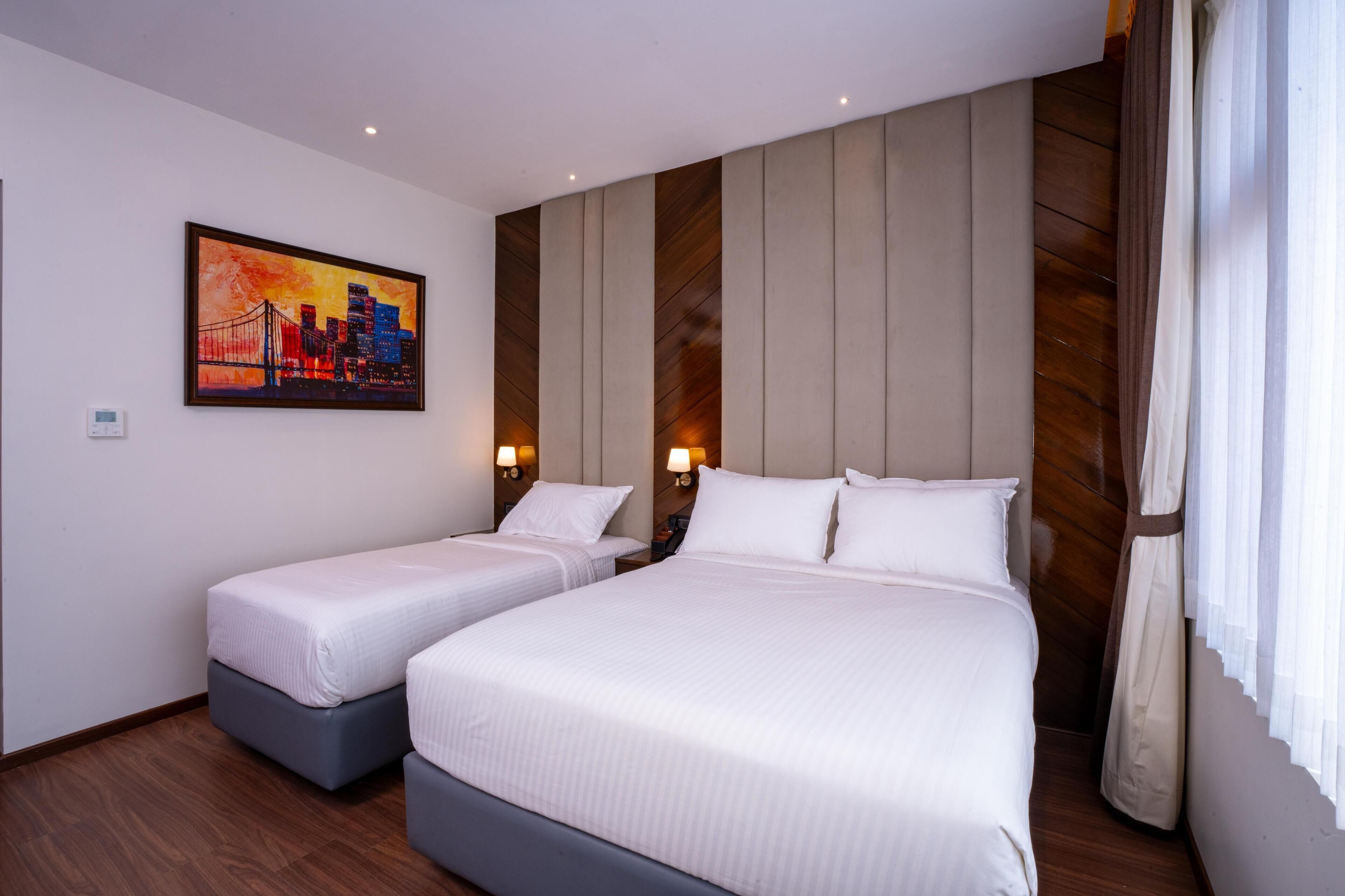 Una habitació d'hotel amb dos llits, un quadre amb un paisatge urbà, panells de fusta i una finestra amb cortines.