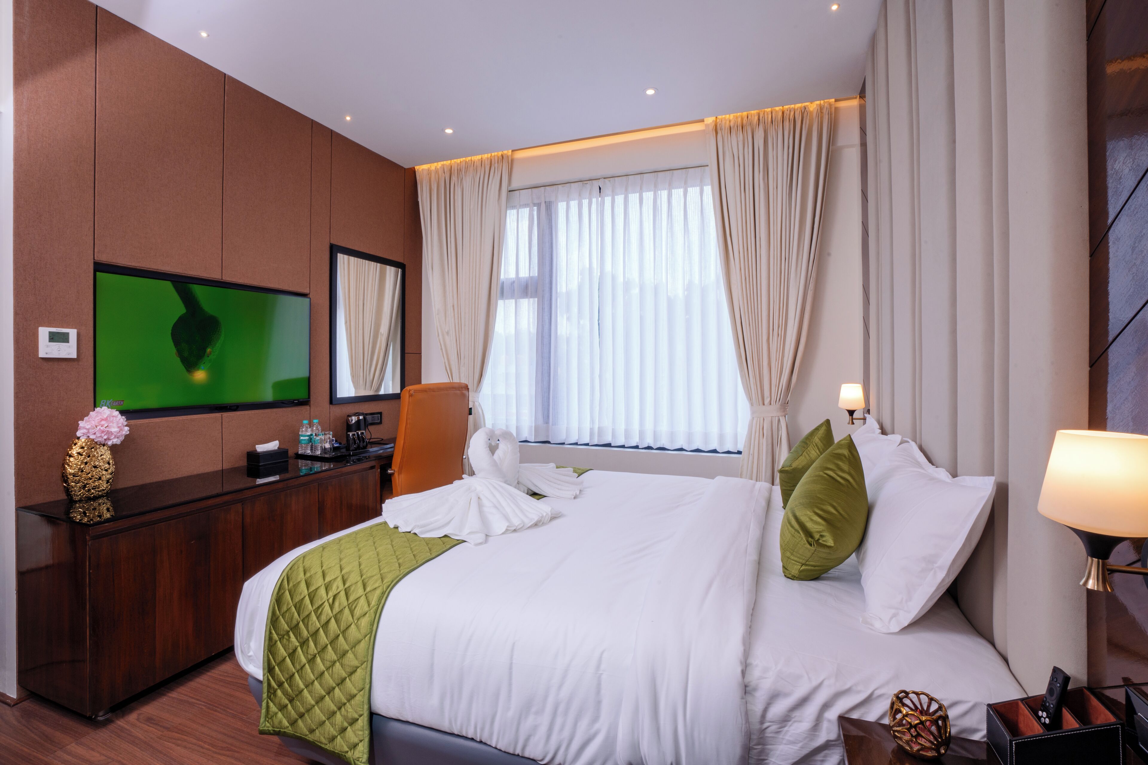 Habitación de hotel con una cama grande, televisor montado en la pared, escritorio con espejo y ventana con cortinas.