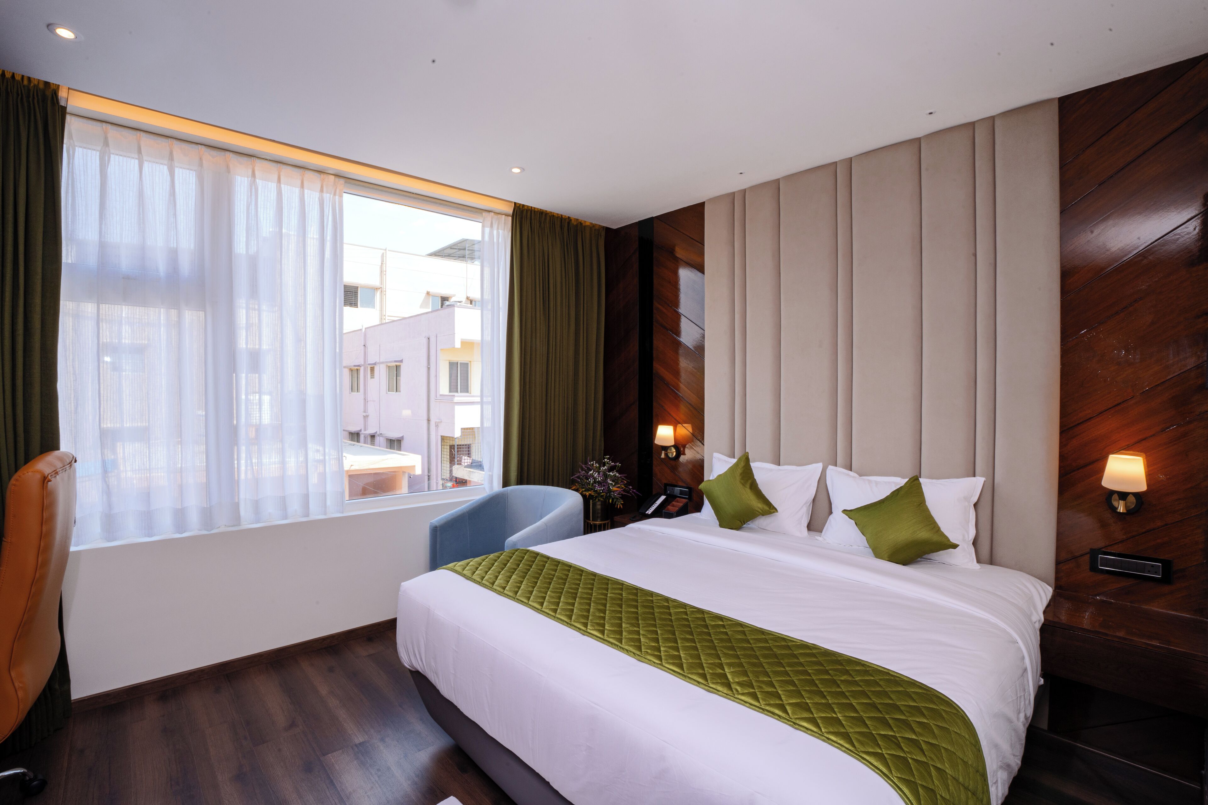 A hotel room with a large bed, a chair, a desk, and a window with curtains.