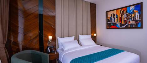 A hotel room with a large bed, a nightstand with a lamp, a chair, and a painting on the wall.