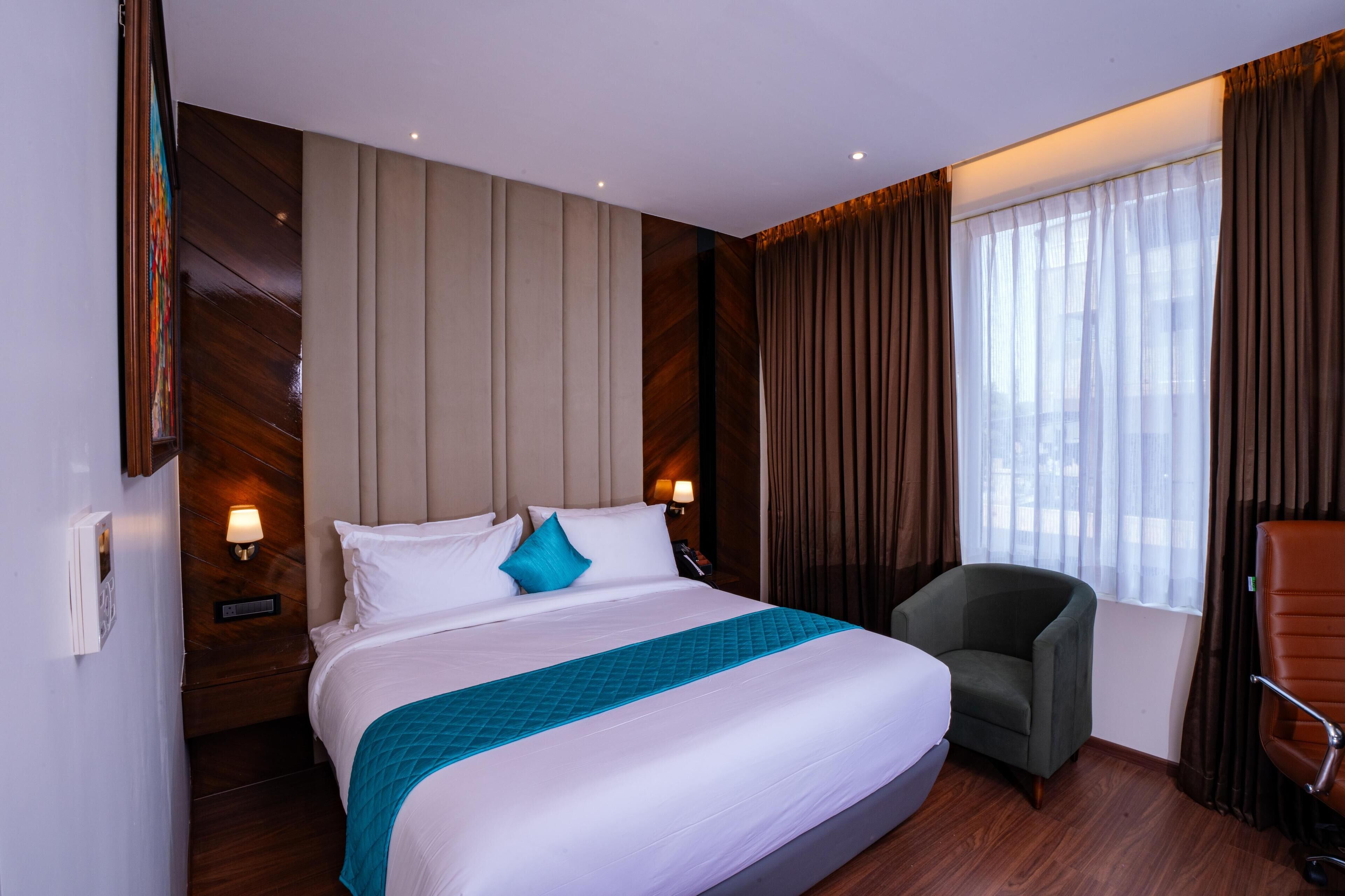 A hotel room with a large bed, a chair, a desk, and a window with curtains.