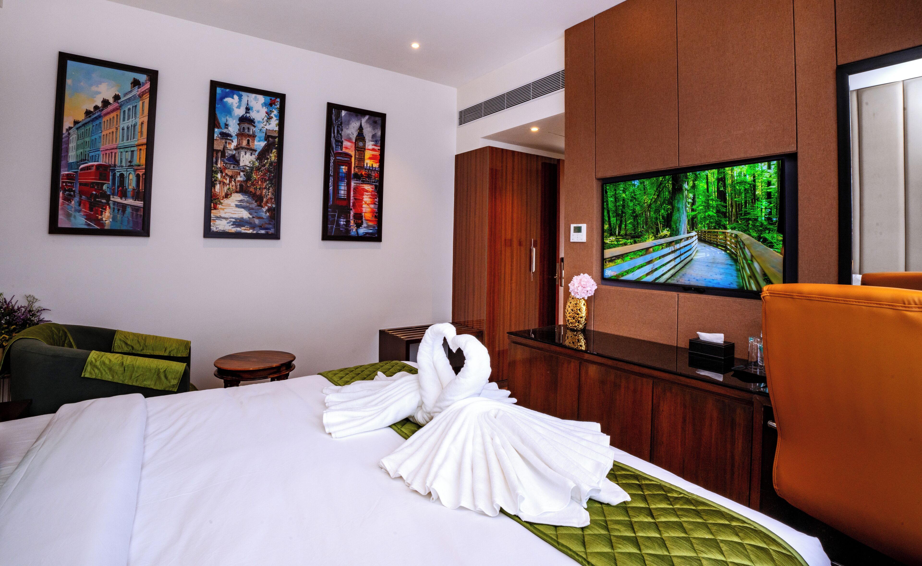 Een hotelkamer met een bed, een televisie en drie ingelijste schilderijen aan de muur.