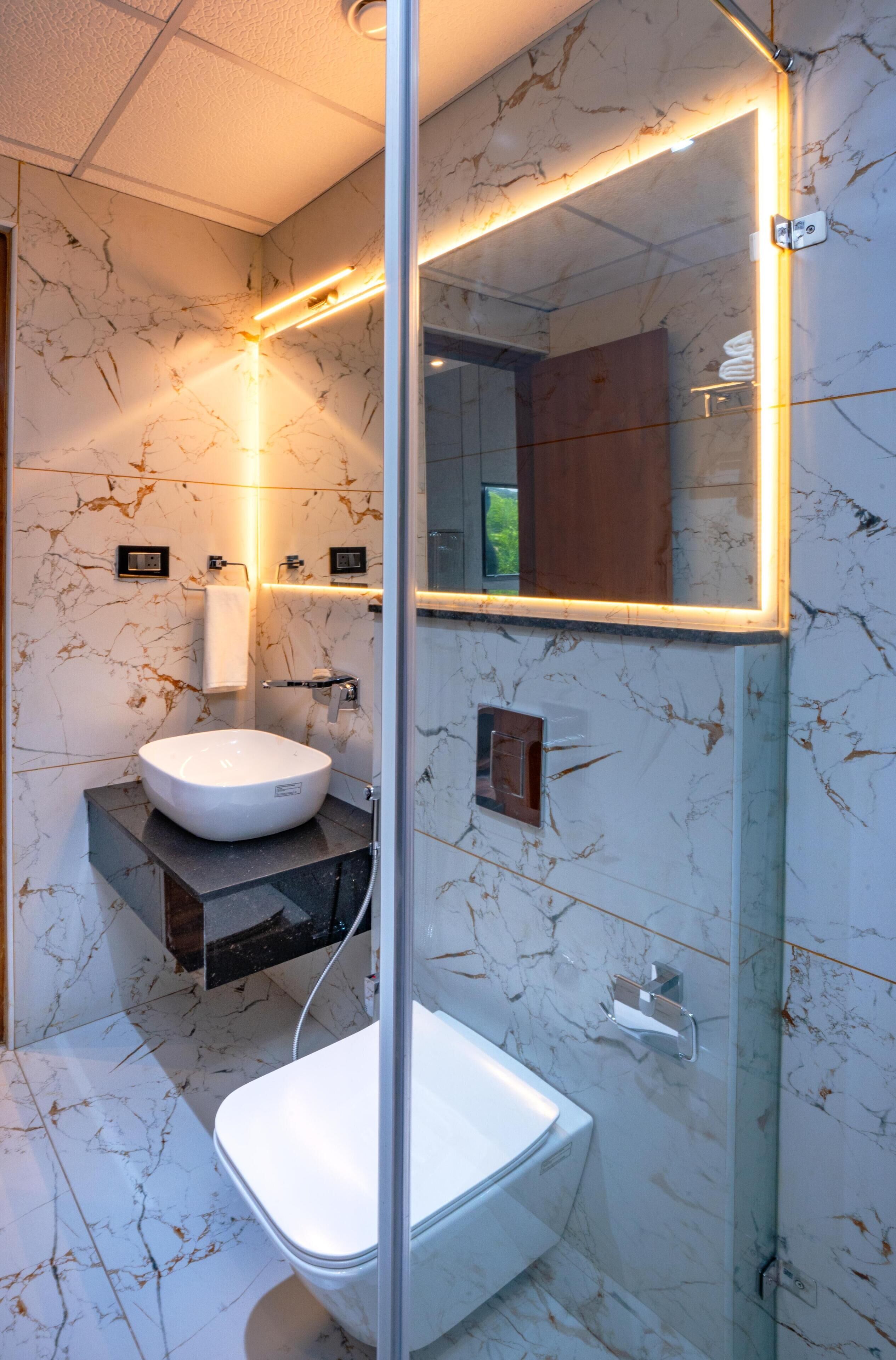 A modern bathroom with a white sink, a glass shower enclosure, and marble-patterned walls.