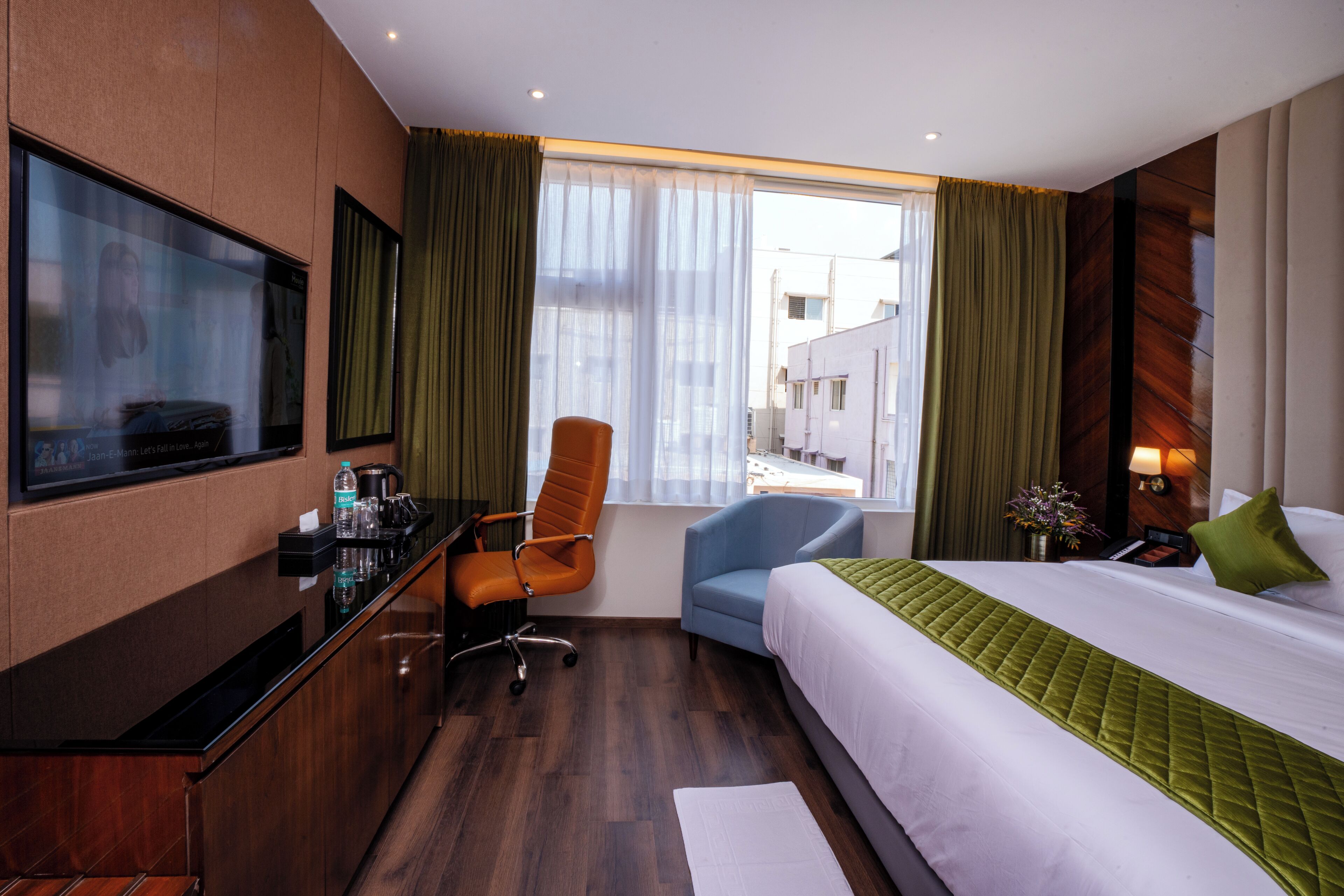Une chambre d’hôtel avec un lit, un bureau, une chaise, une télévision et une fenêtre avec des rideaux.