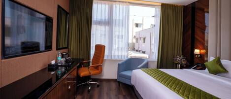 Une chambre d’hôtel avec un lit, un bureau, une chaise, une télévision et une fenêtre avec des rideaux.