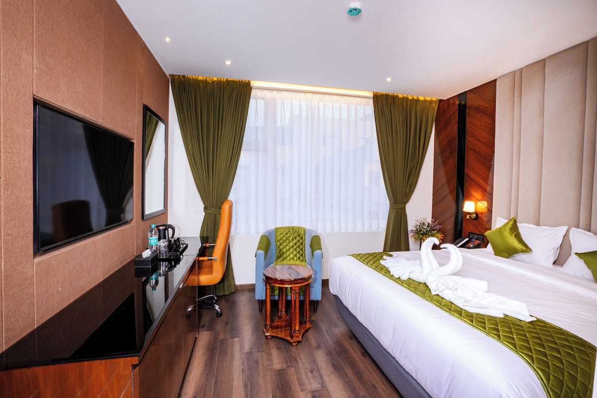 A hotel room with a bed, a TV, a desk with a chair, a small table, and curtains.