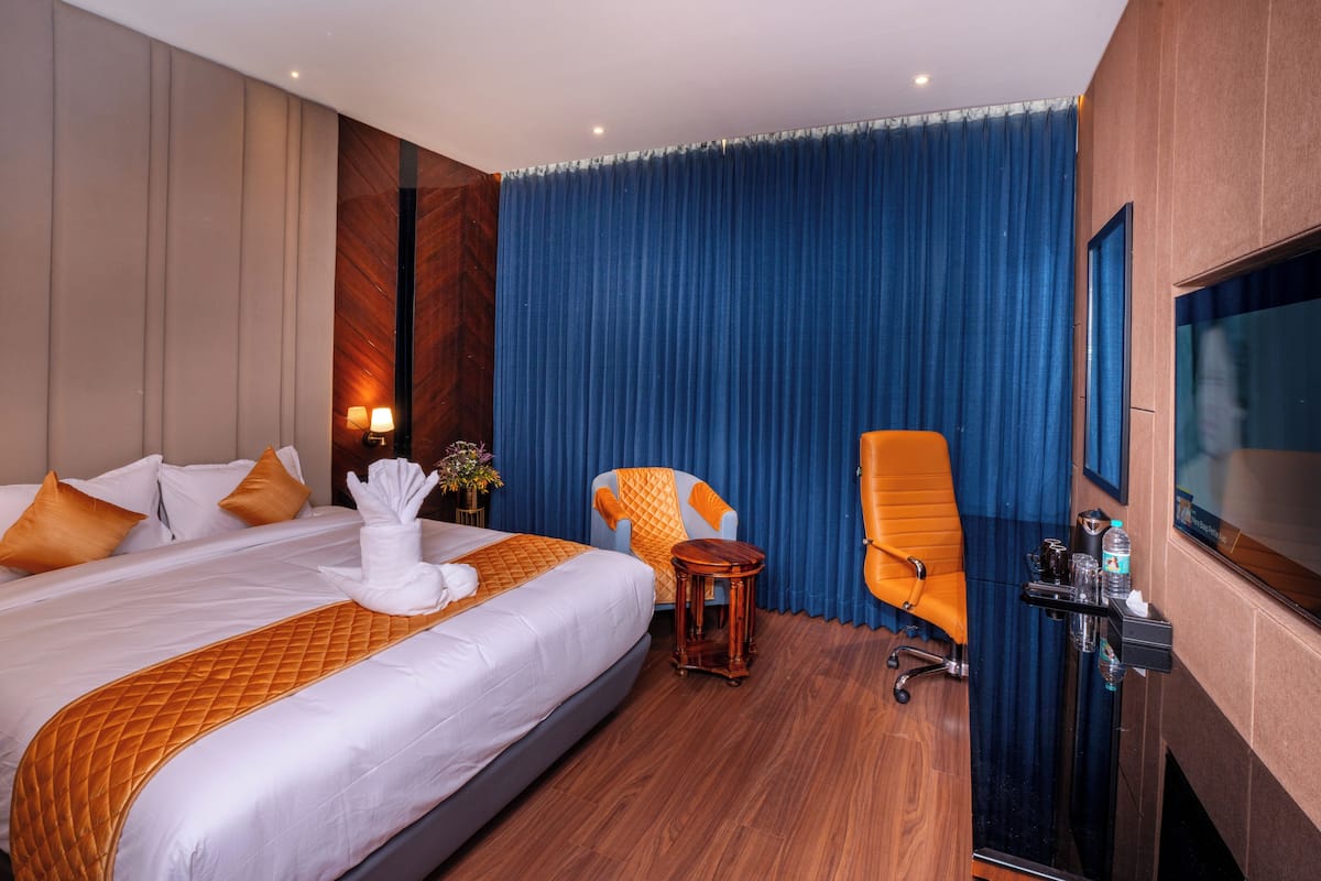 A hotel room with a large bed, two armchairs, a small table, a flat-screen TV, and a minibar.