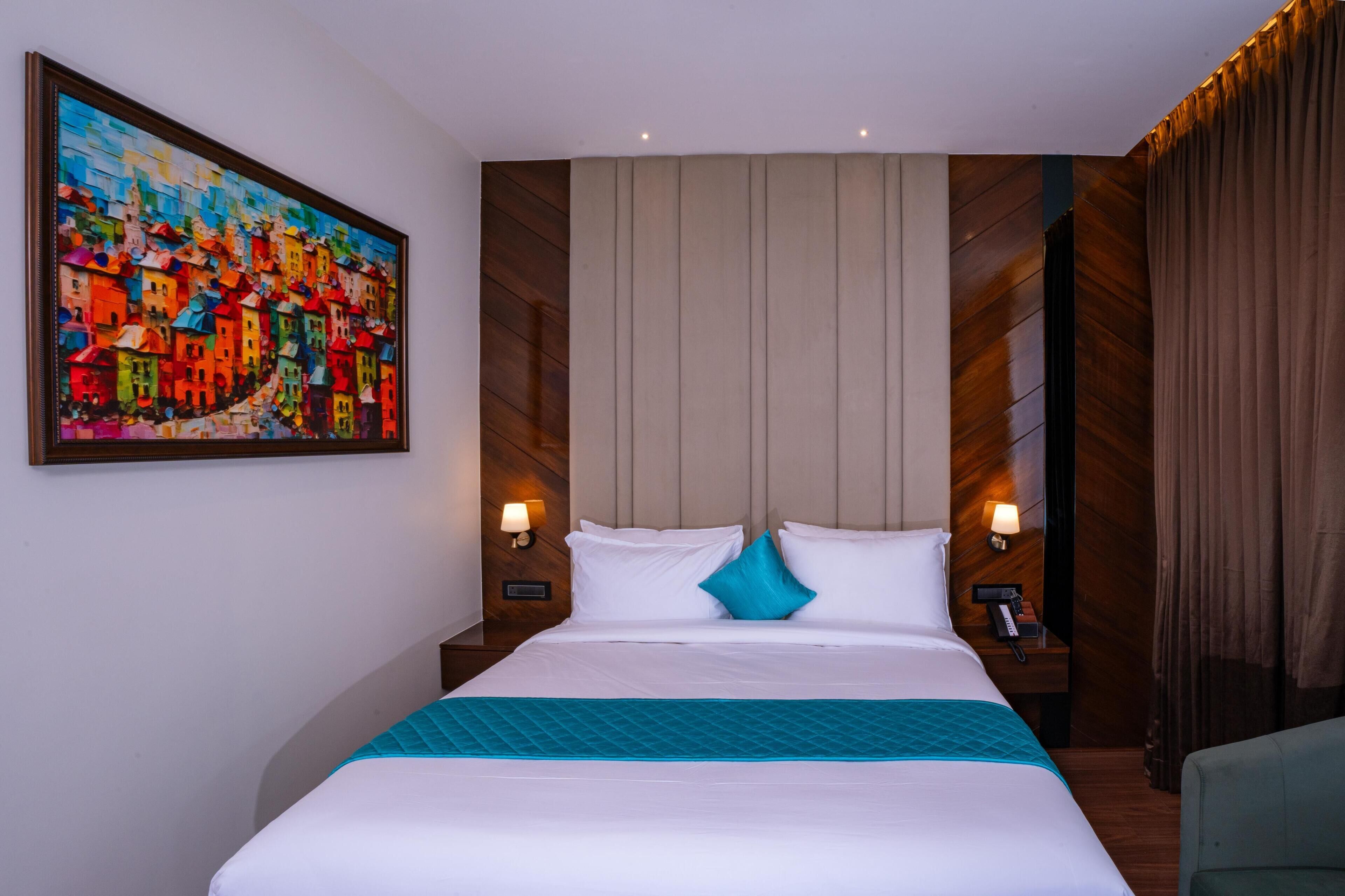 A hotel room with a large bed, two bedside tables with lamps, a painting on the wall, and a curtain on the window.