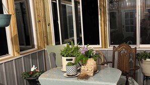 Un coin repas avec une table, des chaises et un lustre. On y trouve des plantes en pot et un panneau d’accueil posé sur la table.