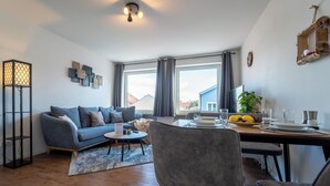 A modern living room with a sofa, dining table, and a large window. - Cozy apartment fully equipped J&K Apartments (Kelheim)