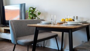 A dining area with a table set for two, a television in the background, and a plant on the side. - Cozy apartment fully equipped J&K Apartments (Kelheim)