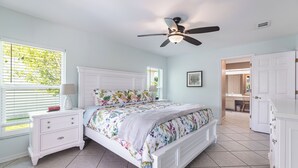 Une chambre à coucher avec un lit, des tables de chevet, un ventilateur de plafond et une vue sur une autre pièce.