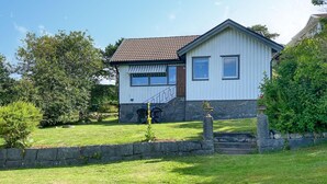 Une maison de plain-pied avec des fondations en pierre, un toit en tuiles et un petit porche à l’avant, avec des marches menant à l’entrée.