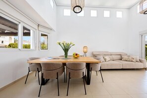 Ein stilvolles Wohnzimmer mit einem beigen Sofa, einem Holzespeisetisch mit vier Stühlen und einem Blumenstrauß.