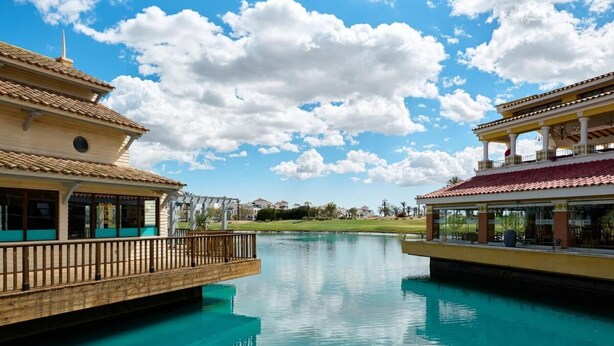 Un hôtel avec une piscine, un pont en bois et un ciel d’un bleu éclatant.