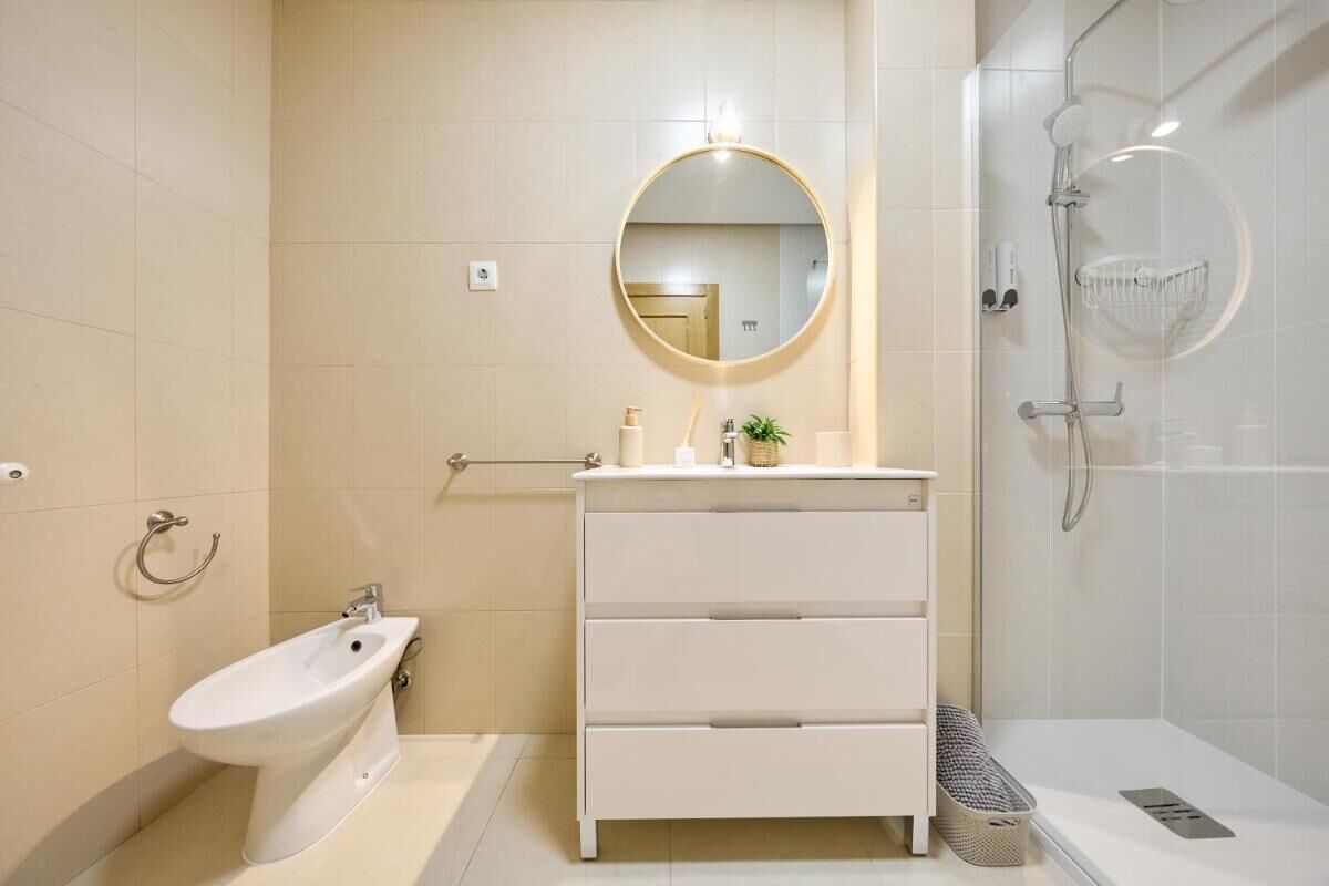 Un baño moderno con un bidé, un tocador blanco con espejo y una zona de ducha.