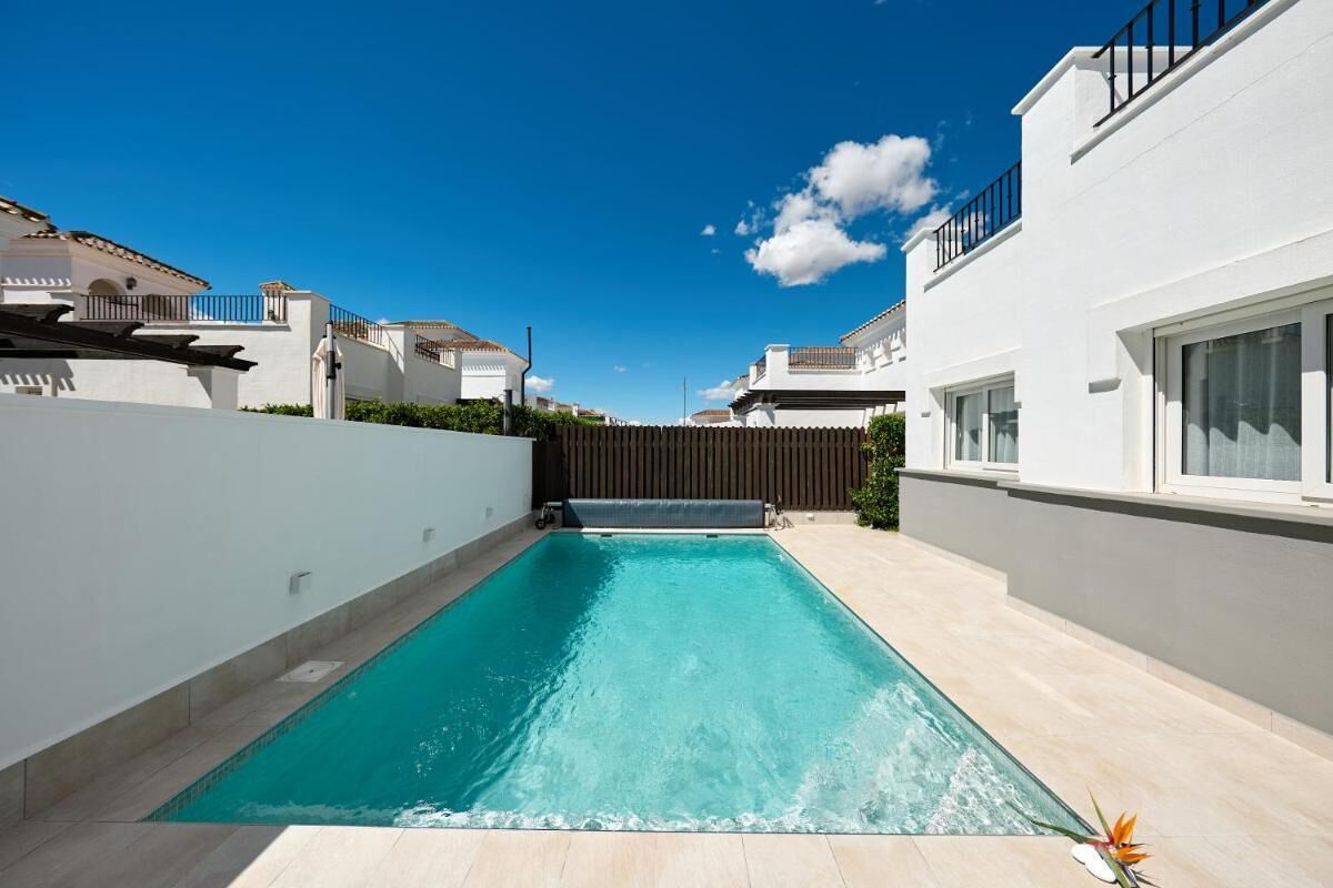 Una piscina rettangolare con acqua cristallina e blu, circondata da muri bianchi e una recinzione in legno.