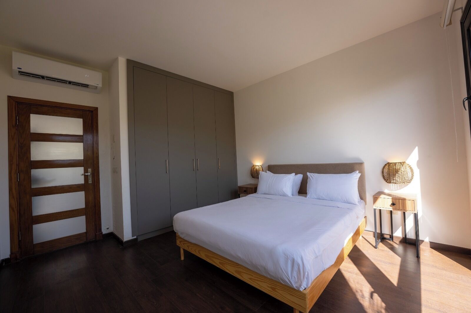 A bedroom with a large bed, wooden wardrobe, and a nightstand with a lamp.
