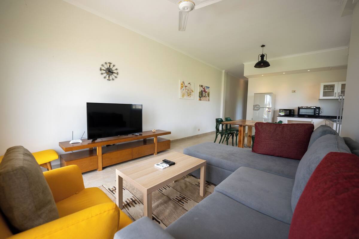 A modern living room with a flat-screen TV, a wooden coffee table, and a grey sofa.