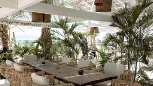 An outdoor dining area with a wooden table and wicker chairs, surrounded by palm trees and under a white pergola. - Stayr Somabay - Bay life home rentals (Soma Bay)