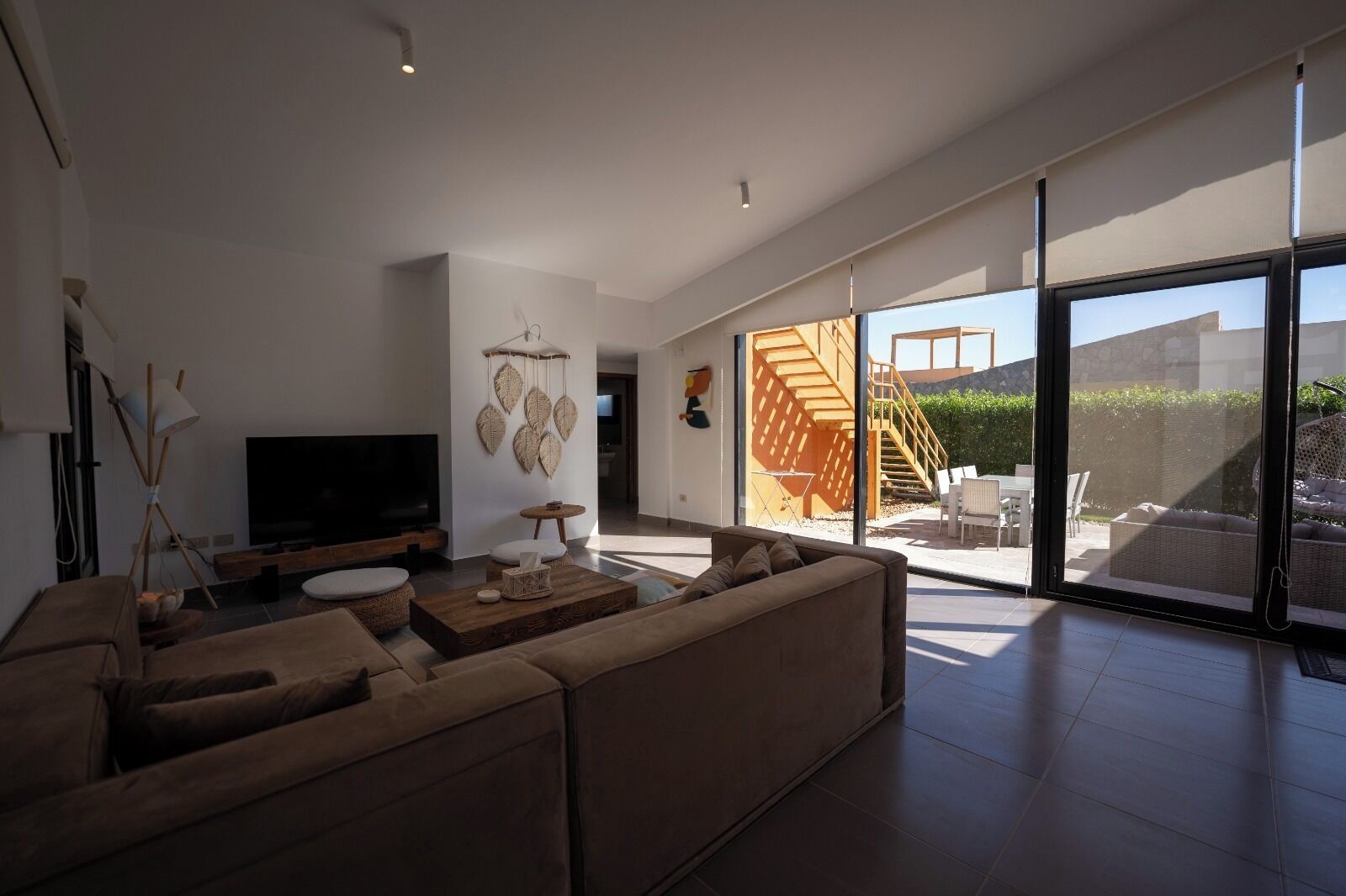 A modern living room with a large TV, comfortable seating, and a view of a staircase leading to an outdoor area.