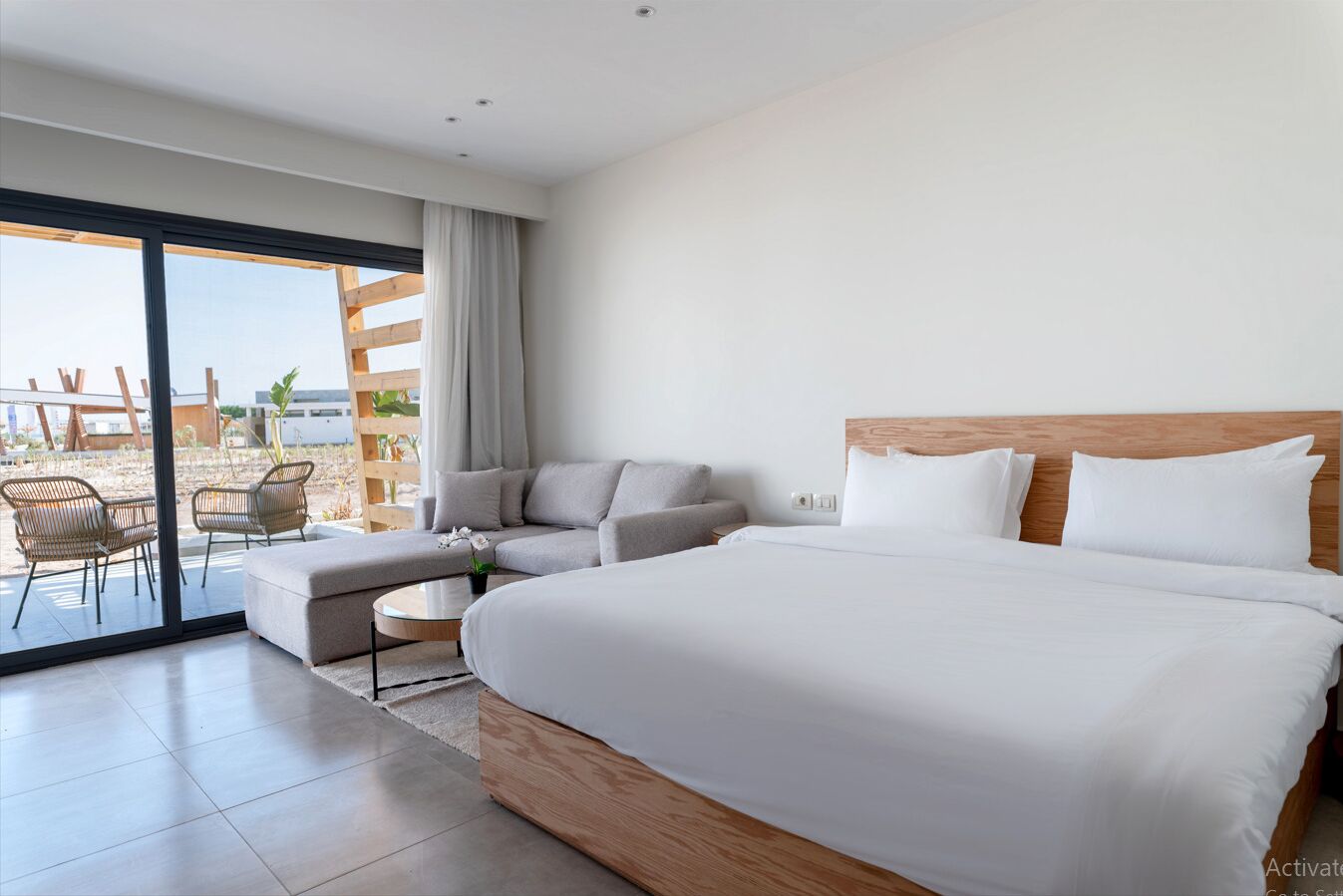 Een moderne hotelkamer met een groot bed, een sofa, een tafeltje en een balkon met zitplaatsen.