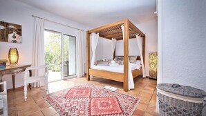 Een slaapkamer met een hemelbed, een bureau, een stoel, een kamerbreed tapijt met een patroon en een rieten mand.
