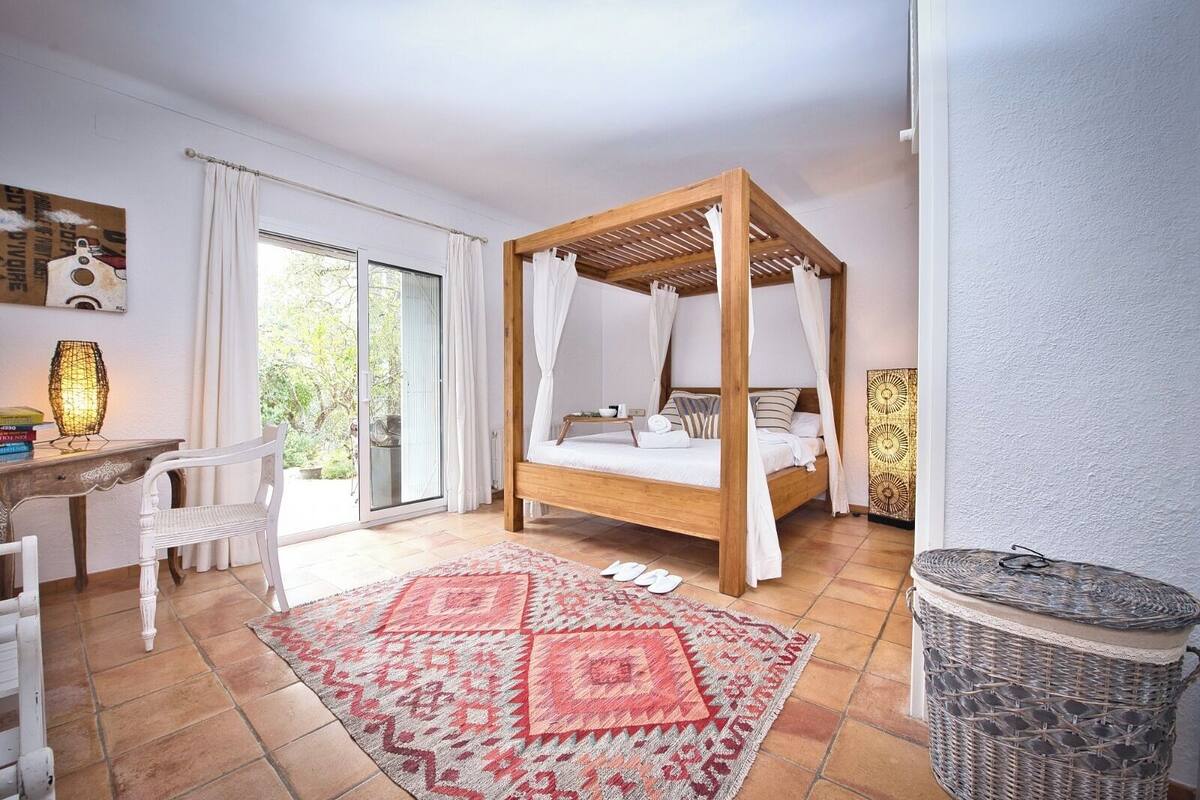 Une chambre à coucher avec un lit à baldaquin, un bureau, une chaise, un tapis à motifs et un panier en osier.