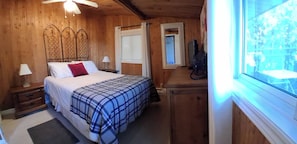 A wooden room with a bed, a nightstand, a dresser, a window, and a ceiling fan.