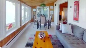 A spacious living area with a wooden ceiling, a grey sofa, a dining table with chairs, and large windows. - Peaceful retreat on the Shores of Lake Erie with access to the lake (Dunnville)