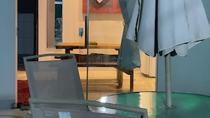 A room with a glass table, a chair, and a partially visible bed.