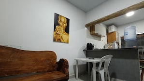 A kitchenette with a coffee maker, a water dispenser, and a refrigerator. There is a wooden bench and a white table with two chairs.