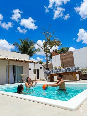 Ein Swimmingpool mit gefliestem Deck, einer Holzbank und einer Palme im Hintergrund.