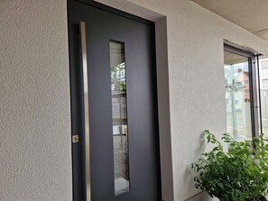 A modern door with a vertical handle, a textured wall, and a window with a view of buildings.