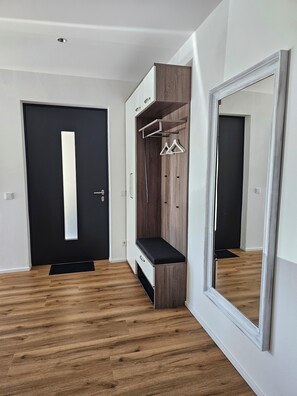 Ein modernes Zimmer mit einer schwarzen Tür, einer Holzbank, einem Schrank mit Spiegel und einem großen Wandspiegel.