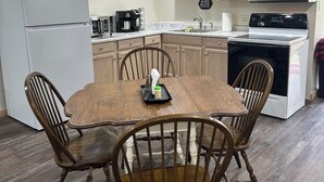 A compact kitchen with a dining table, wooden chairs, a refrigerator, a microwave, a coffee maker, and a sign that says "BE OUR GUEST". - Charming pet friendly 1-bedroom apartment with WiFi, AC in quaint Conneaut Lake (Conneaut Lake)