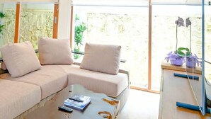 A modern living room with a sectional sofa, a coffee table with a natural wood top, and a glass cabinet with a lamp. - D'Kamboja KIS1 Managed by D'Kamboja Group (Bali)