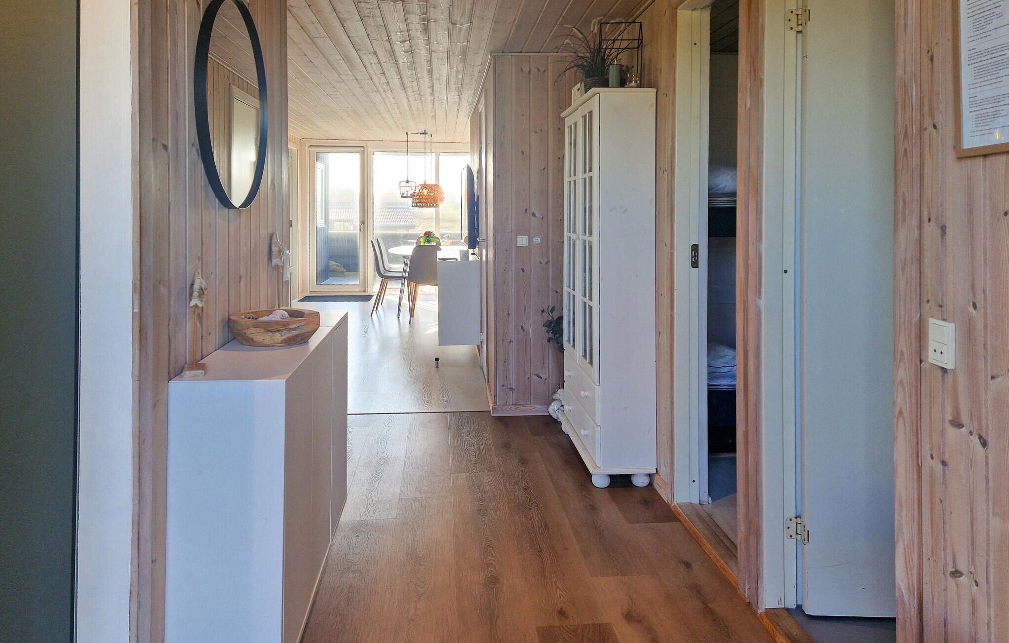 Un couloir intérieur aux murs en bois, avec un meuble blanc, un réfrigérateur blanc et un banc en bois.
