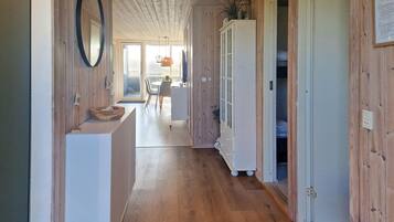 Un couloir intérieur aux murs en bois, avec un meuble blanc, un réfrigérateur blanc et un banc en bois.