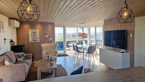 A modern living room with a sofa, coffee table, and TV, wooden ceiling, and large windows. - Gorgeous home in Løkken with sauna (Løkken)