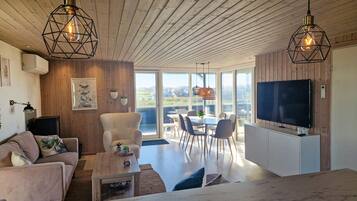 Un salon moderne avec un canapé, une table basse et un téléviseur, un plafond en bois et de grandes fenêtres.