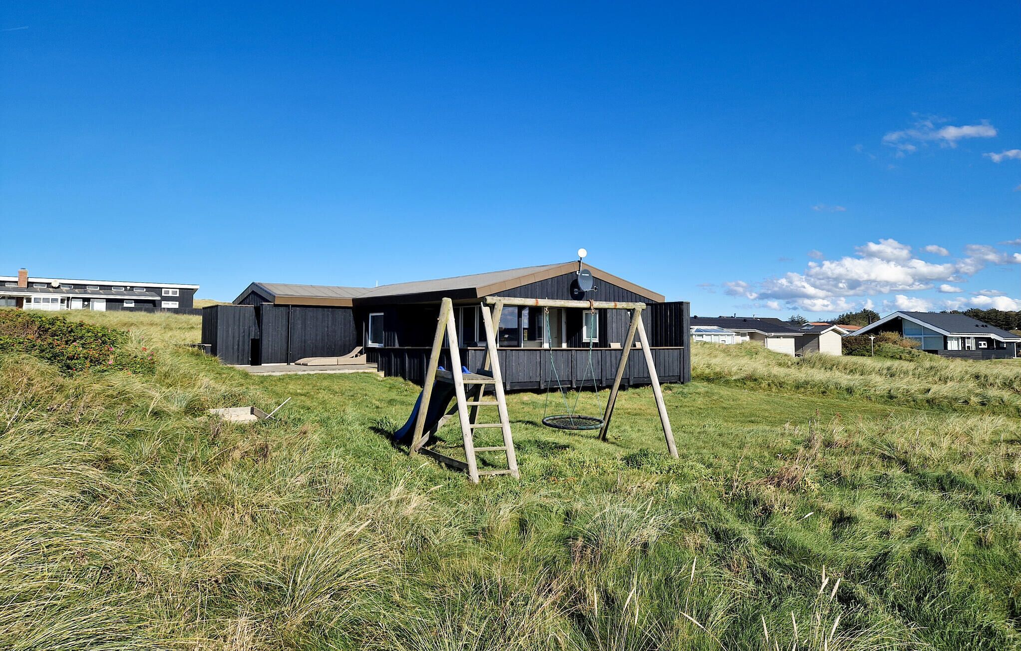 Una casa moderna con un porche amplio y un columpio en un campo cubierto de césped.