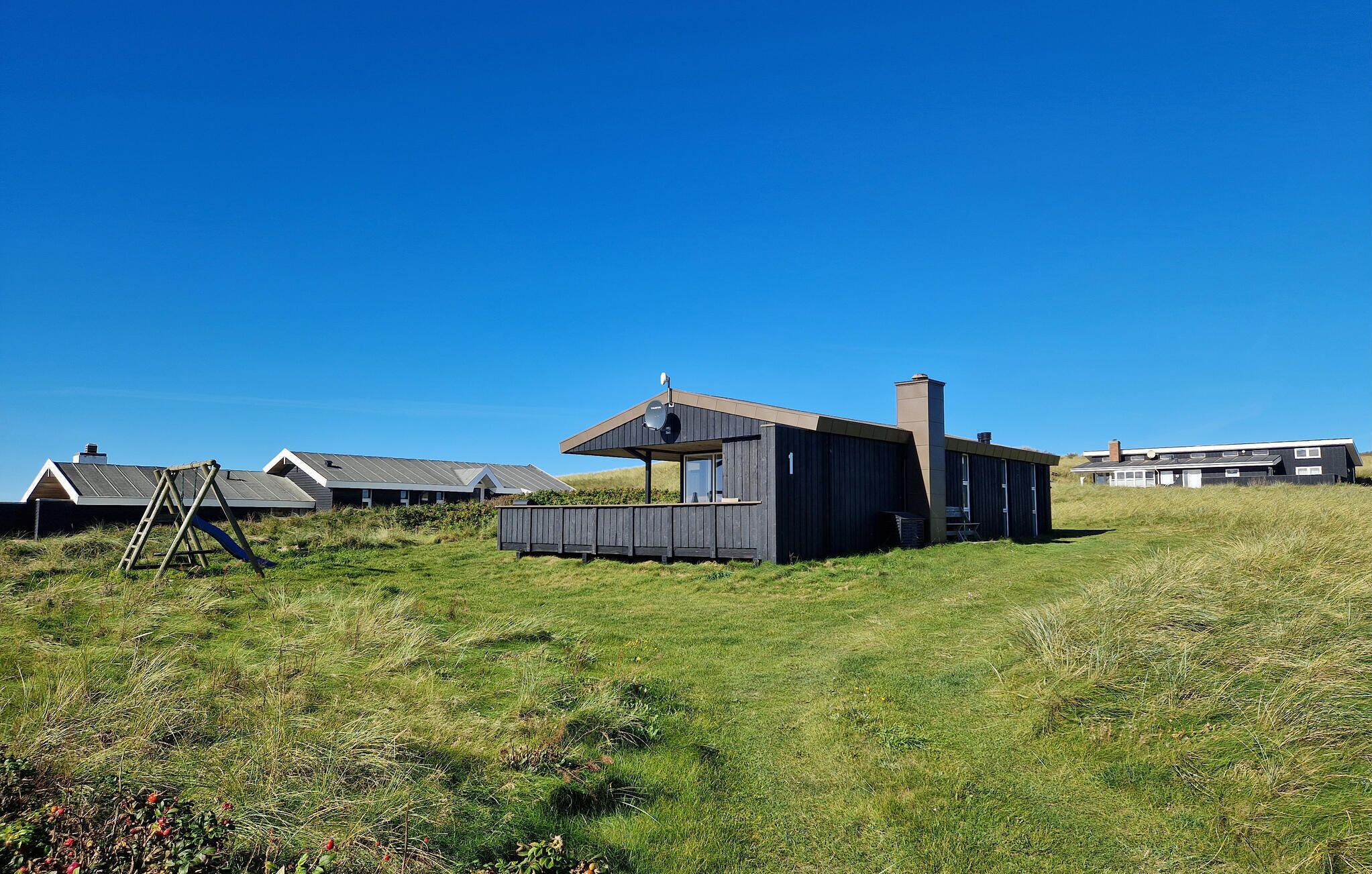 Un bâtiment moderne, de plain-pied, doté d’un toit en pente et d’une cheminée, entouré d’un champ herbeux et d’autres constructions similaires.