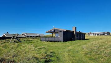 Un bâtiment moderne, de plain-pied, doté d’un toit en pente et d’une cheminée, entouré d’un champ herbeux et d’autres constructions similaires.