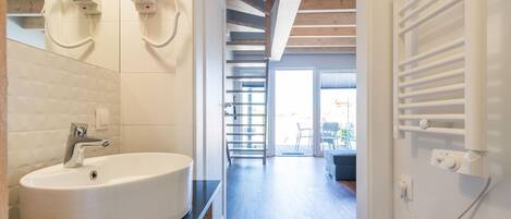 A modern bathroom with a large white sink, a hairdryer mounted on the wall, and a walk-in shower with a glass door.