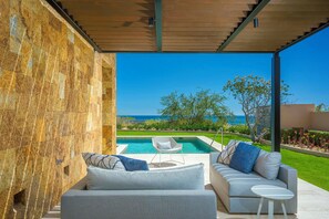Un área de estar moderna al aire libre con piscina, un muro de piedra y vistas al mar.
