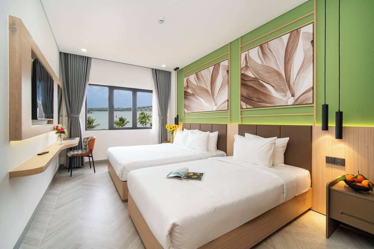 Habitación de hotel con dos camas, un escritorio, una silla, un ventanal con vistas y una pared con diseño de hojas.