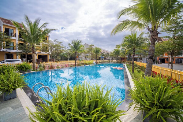 A swimming pool surrounded by palm trees and a yellow fence, with buildings in the background.