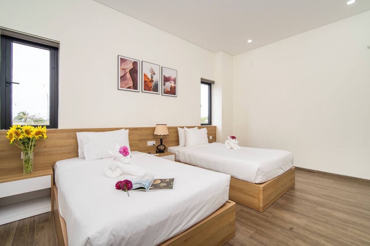 Habitaci ón de hotel con dos camas, una mesita de noche con lámpara, un florero con flores y cuadros en la pared.